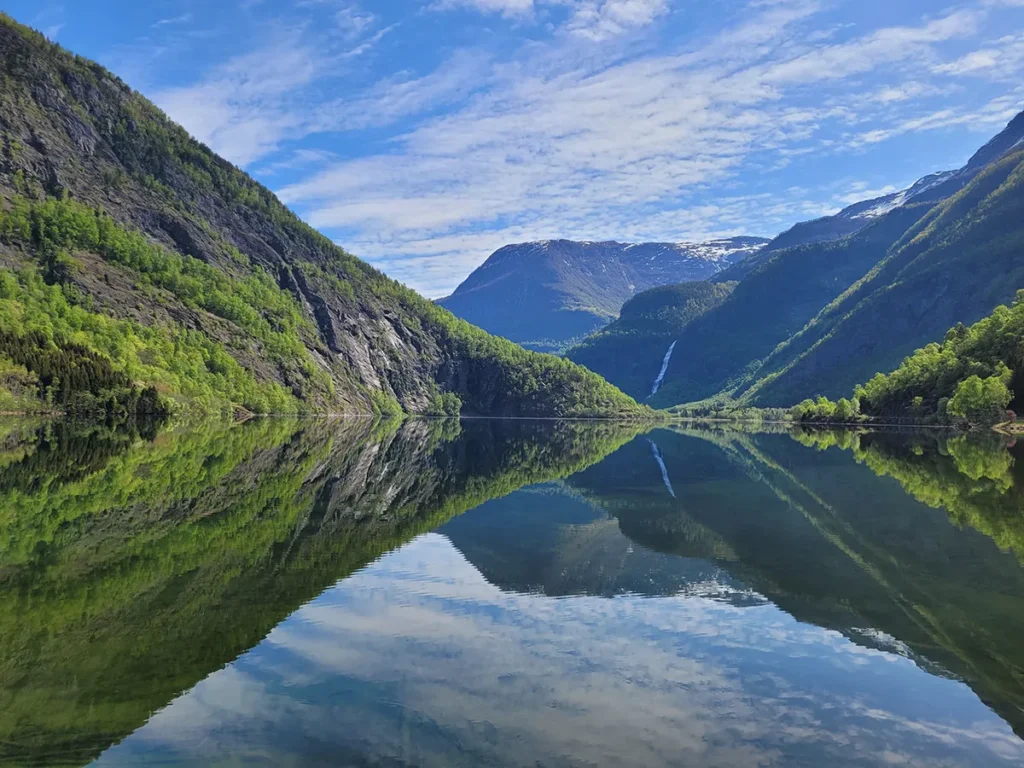 Panoramic view of Eidsvatnet lake in Luster, Norway, with green mountains reflecting on the calm water surface.