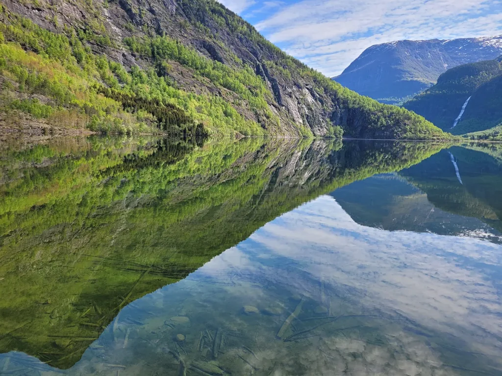 Scenic landscape shot of Eidsvatnet lake focusing on high mountain peaks and light clouds reflecting on clear water.