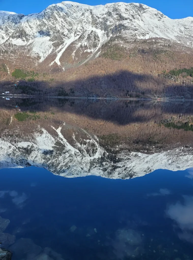 Spring landscape in Norway featuring snowy mountains of Lustrafjorden with fresh green growth emerging in the foreground.