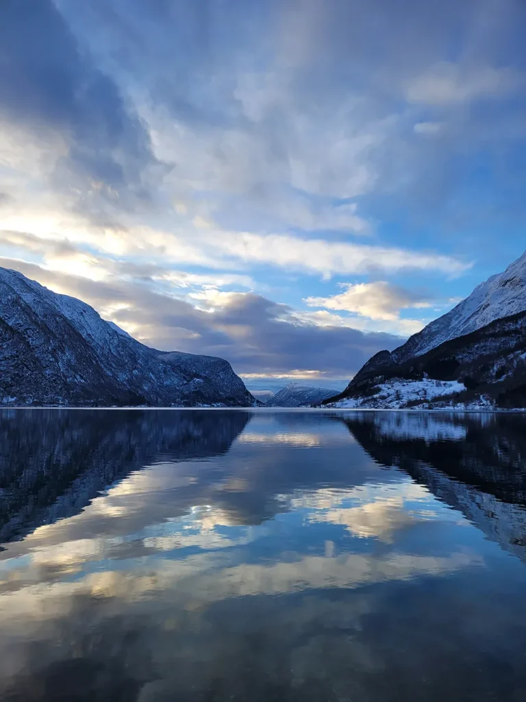 Wide panoramic view of Lustrafjorden under a clear blue summer sky with massive mountain peaks in Norway.
